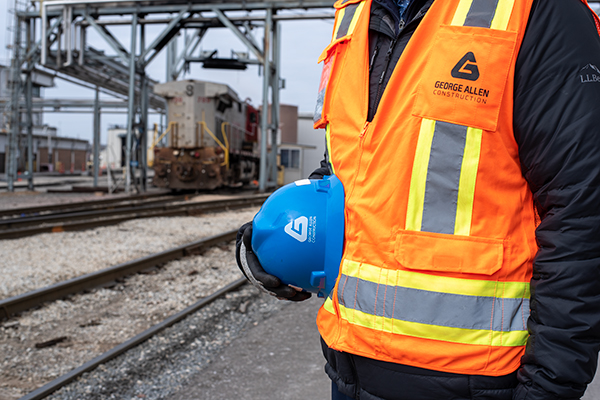 Construction worker holding hard hat with train locomotive in background.