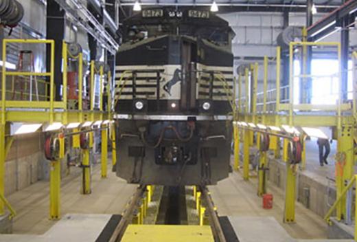 Railroad car hovers over maintenance pit.