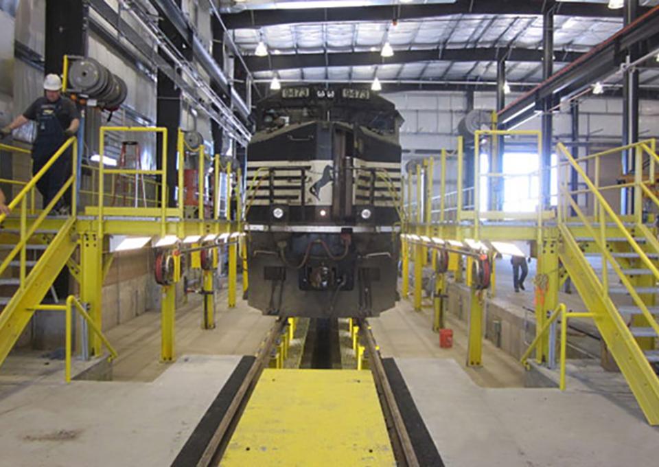 Railroad car hovers over maintenance pit.