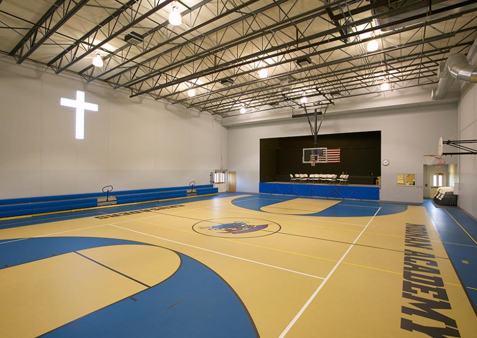 Gymnasium interior and basketball court with yellow and blue flooring and a cross-shaped window.