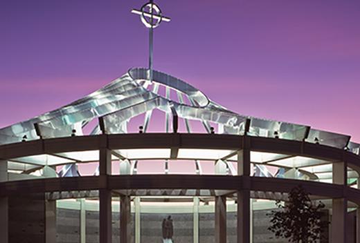 Circular mausoleum chrome dome with a cross, illuminated at night.