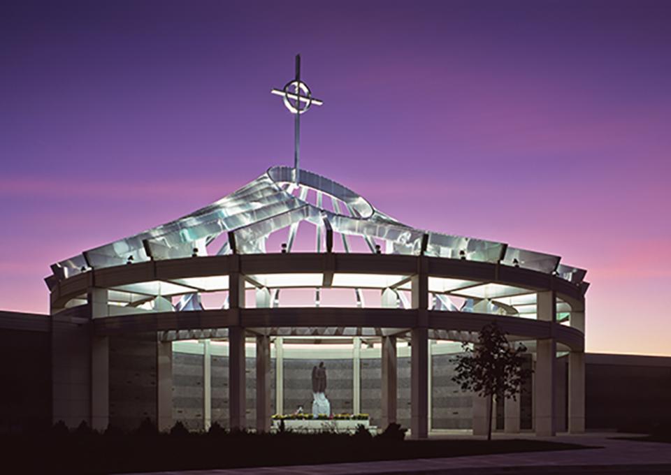 Circular mausoleum chrome dome with a cross, illuminated at night.