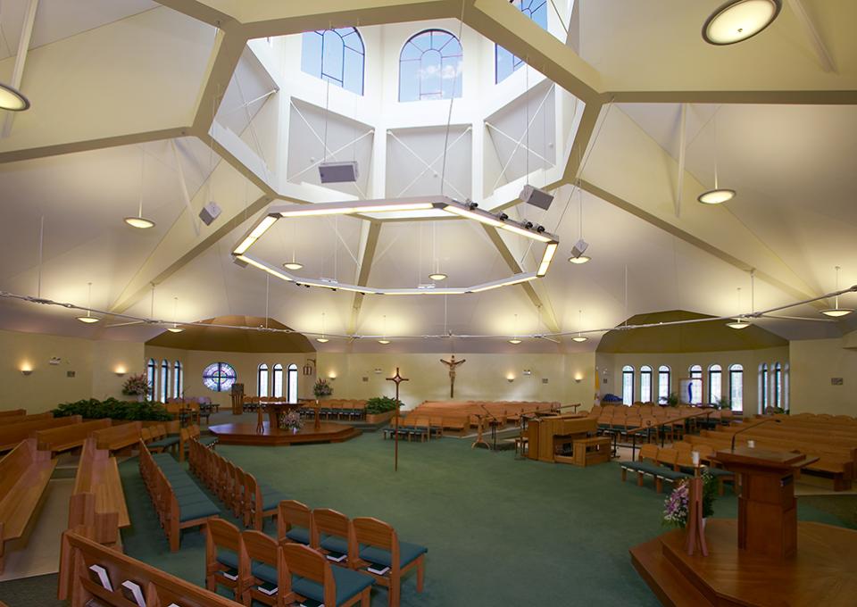 Interior worship space with wooden pews, green carpet, and octagonal skylight.